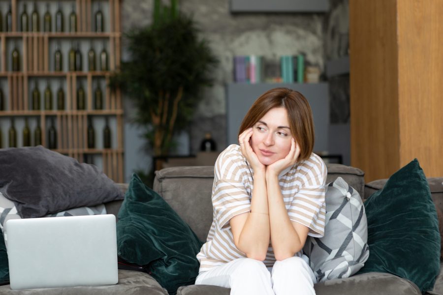 Unhappy woman sits on the couch after working on laptop at home.