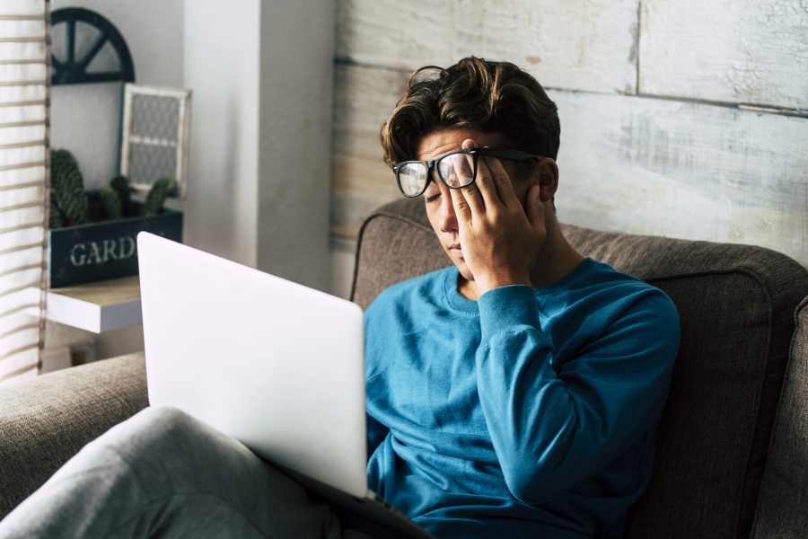 Stressed student at home studying with personal laptop computer - tired teenager for school work -internet. addiction for game or job search concept - indoor technology activity