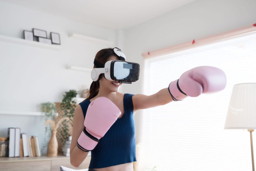 Young Asian woman fighter boxer fit girl in VR glasses wearing boxing gloves playing a boxing game at home.